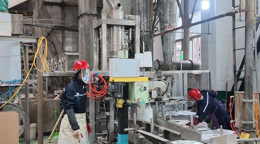 Workers operating an ammonium persulfate packaging line at a chemical production facility